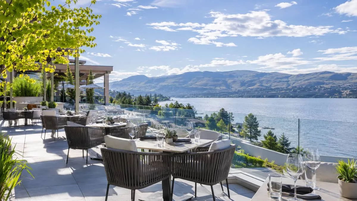 an outdoor resort terrace overlooking Okanagan Lake with commercial-grade patio furniture, wine glasses on tables, warm 