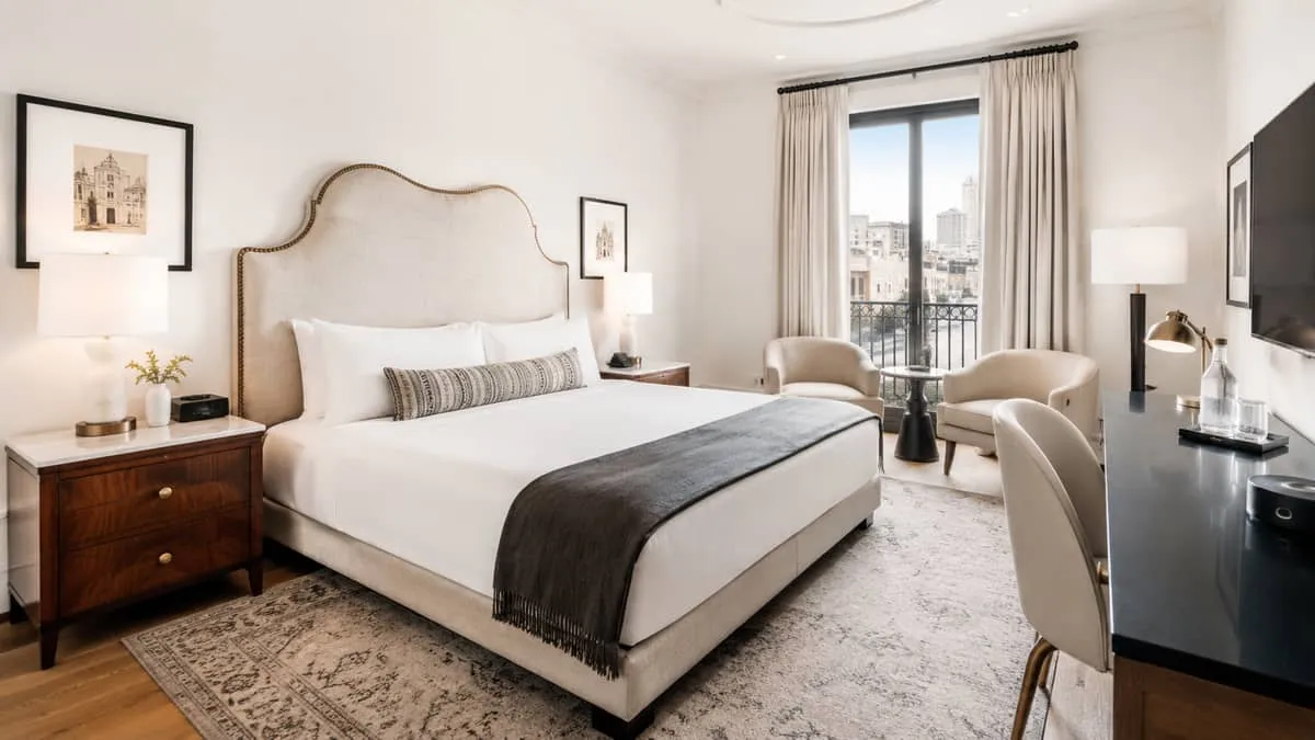 a hotel room with a mix of custom upholstered headboard and vintage-inspired side tables, showing the layered, collected