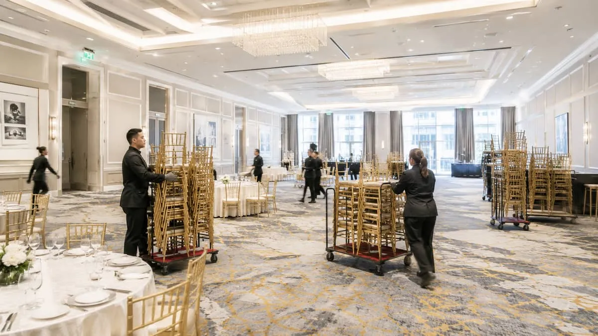 hotel banquet staff stacking chiavari chairs onto rolling carts in a large Ottawa ballroom, mid-flip between a seated di
