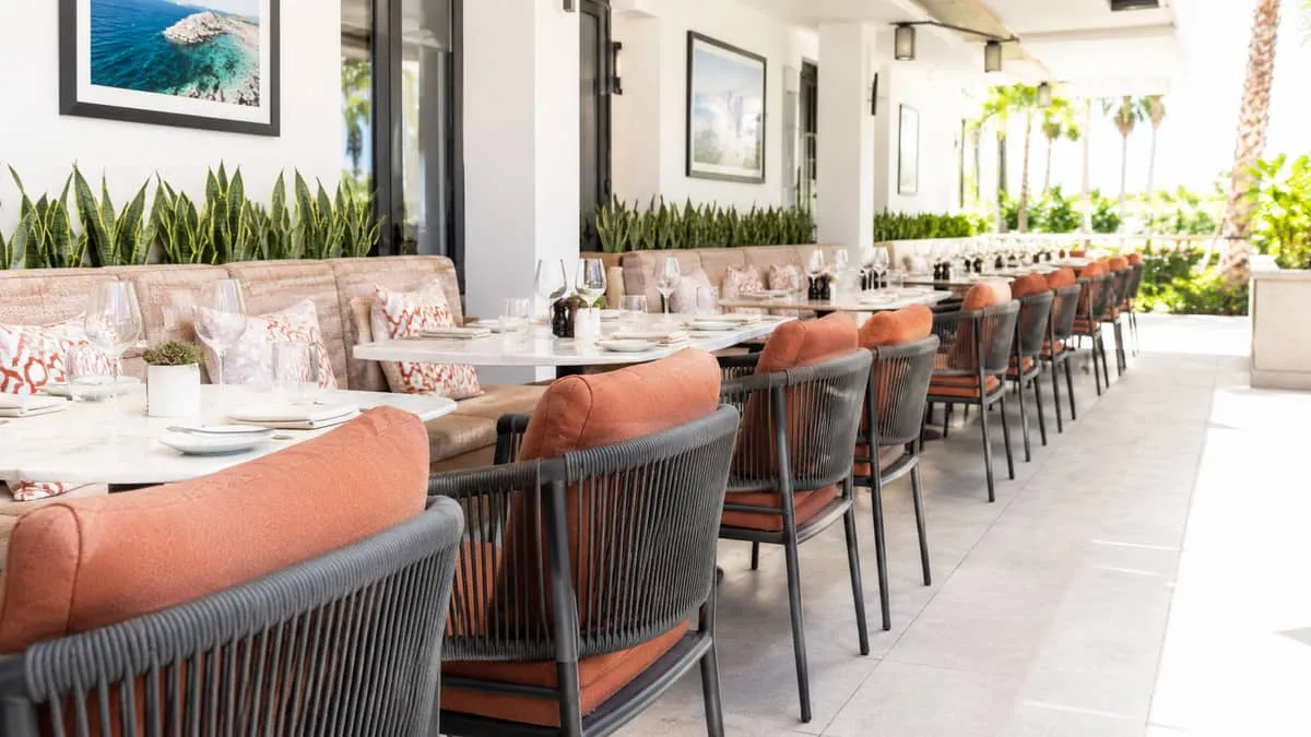 row of commercial outdoor dining chairs with Sunbrella fabric cushions in a warm terracotta or sand tone, arranged on a 