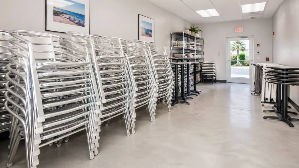 stacked commercial aluminum patio chairs in an organized storage room, showing efficient stacking with protective caps o