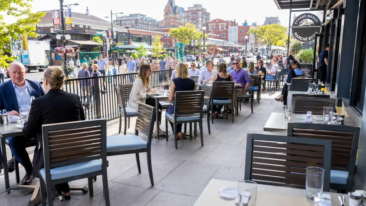 a busy Byward Market restaurant patio in Ottawa showing commercial-grade metal and wood chairs with upholstered seats at