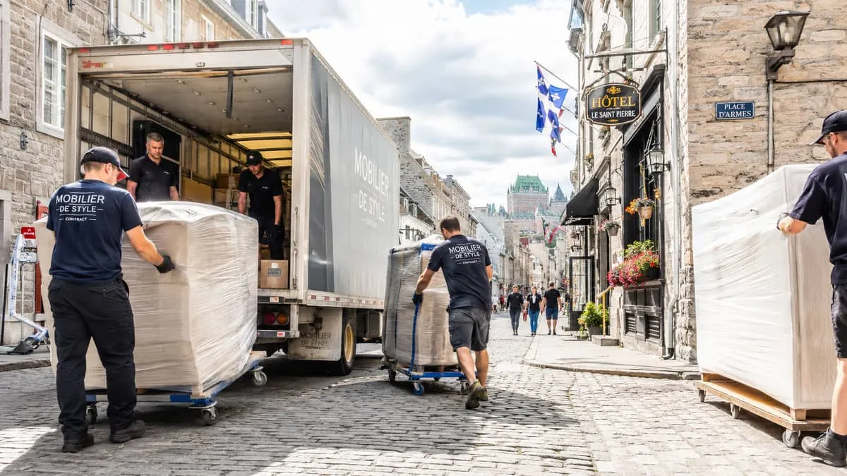 furniture delivery crew unloading contract hotel furniture from a truck on a narrow Old Quebec cobblestone street, showi