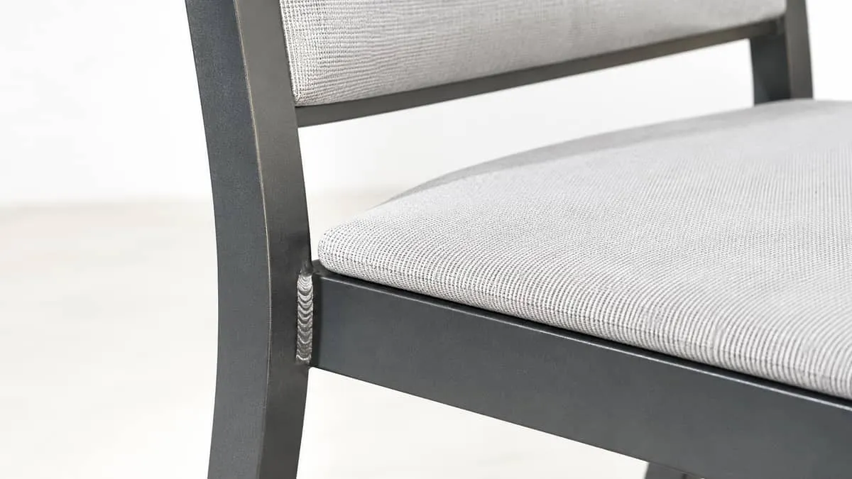 close-up of a contract-grade restaurant chair showing welded frame joint and upholstered seat, photographed on a light b