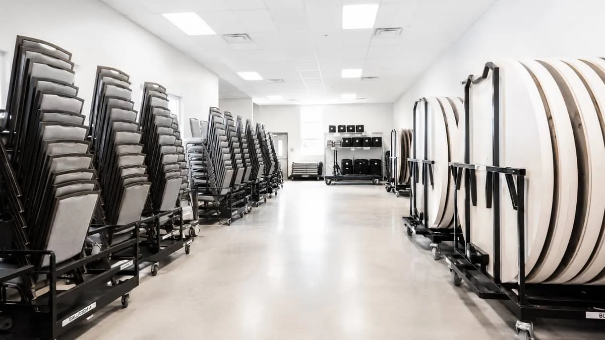 a well-organized event venue storage room showing chairs on trolleys and folded tables stacked vertically on carts, repr
