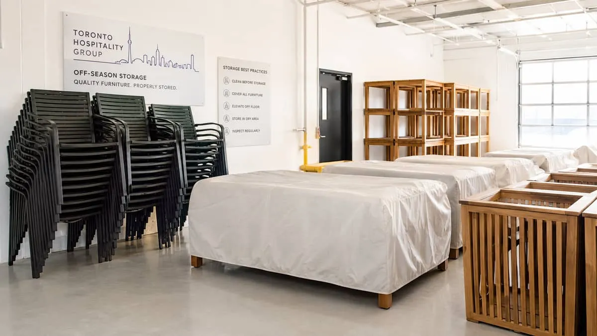 organized off-season storage scene showing stacked commercial patio chairs and covered teak furniture in a clean restaur