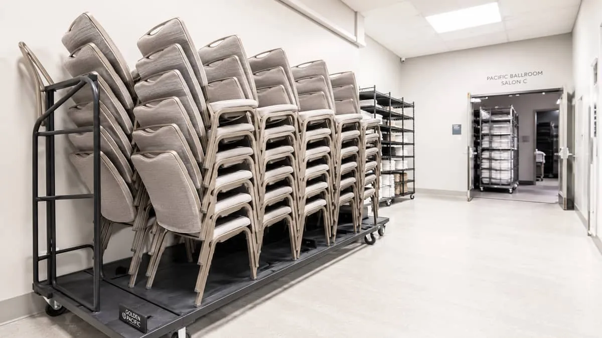 rows of stackable upholstered banquet chairs stored neatly on a rolling dolly in a hotel storage room, showing how effic