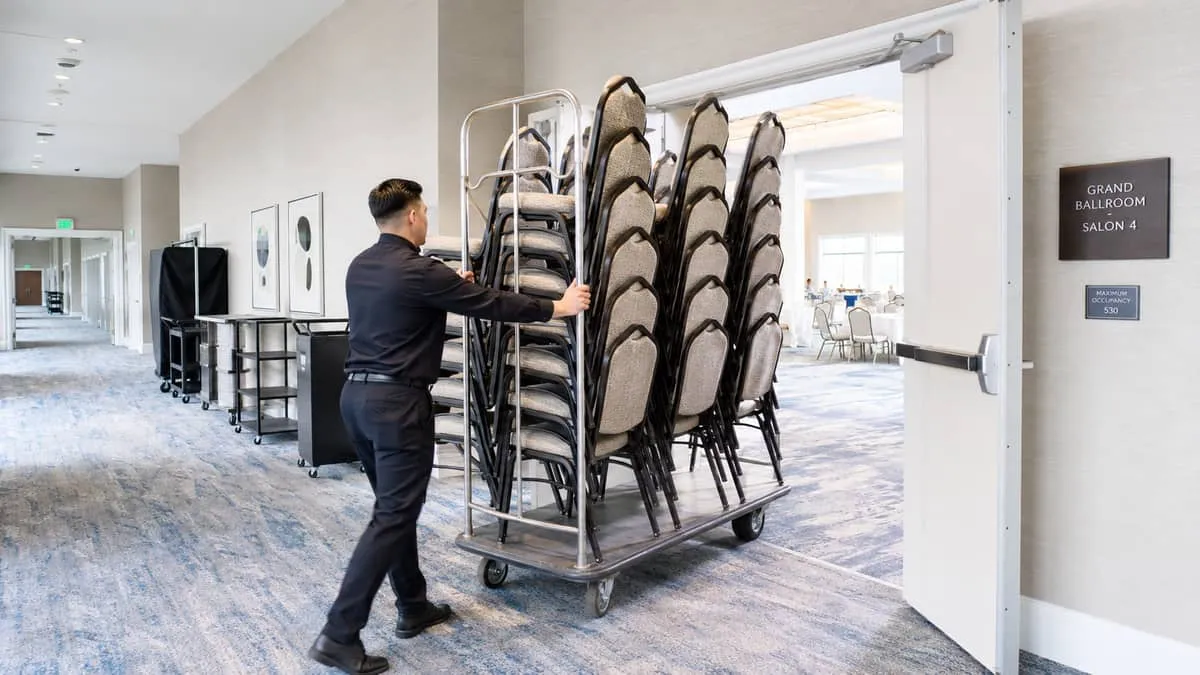 hotel banquet staff rolling a fully loaded chair cart through a service corridor, showing the logistics of moving banque