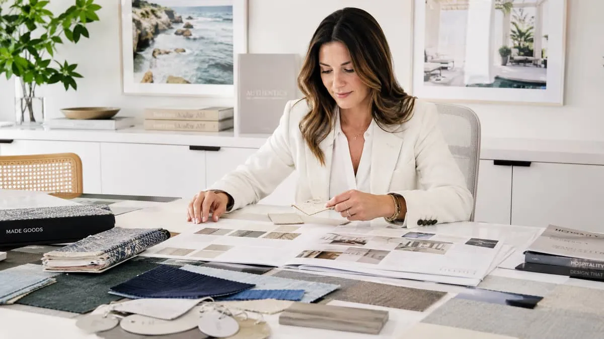 interior designer or procurement consultant reviewing fabric and finish samples at a desk, with specification sheets and