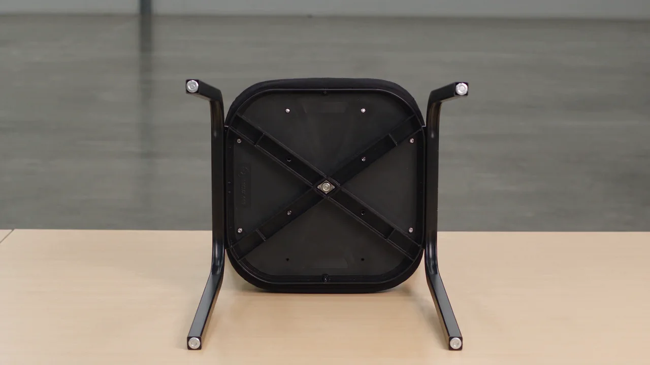 The underside of a commercial stacking chair turned over on the floor, showing the cross-braced steel frame and glide feet
