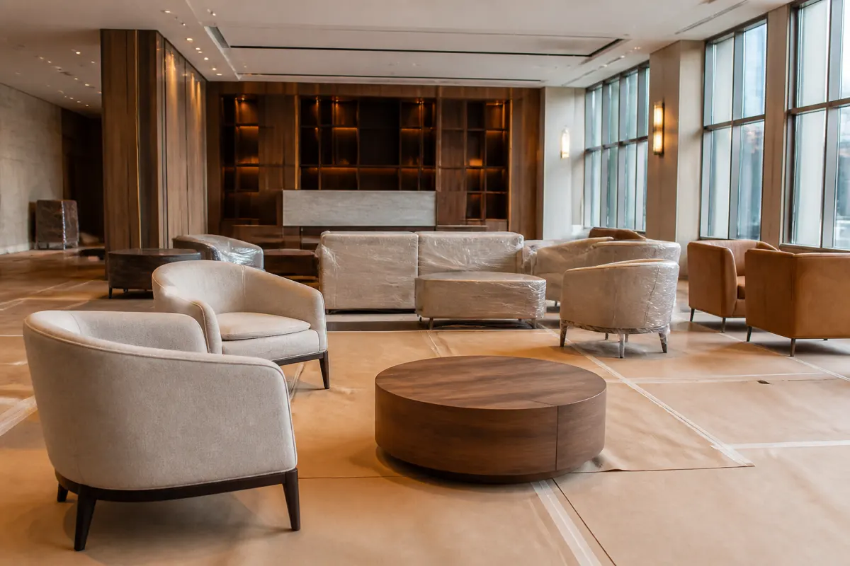 Hotel space mid furniture installation, new seating pieces staged on protective floor covering, orderly and bright