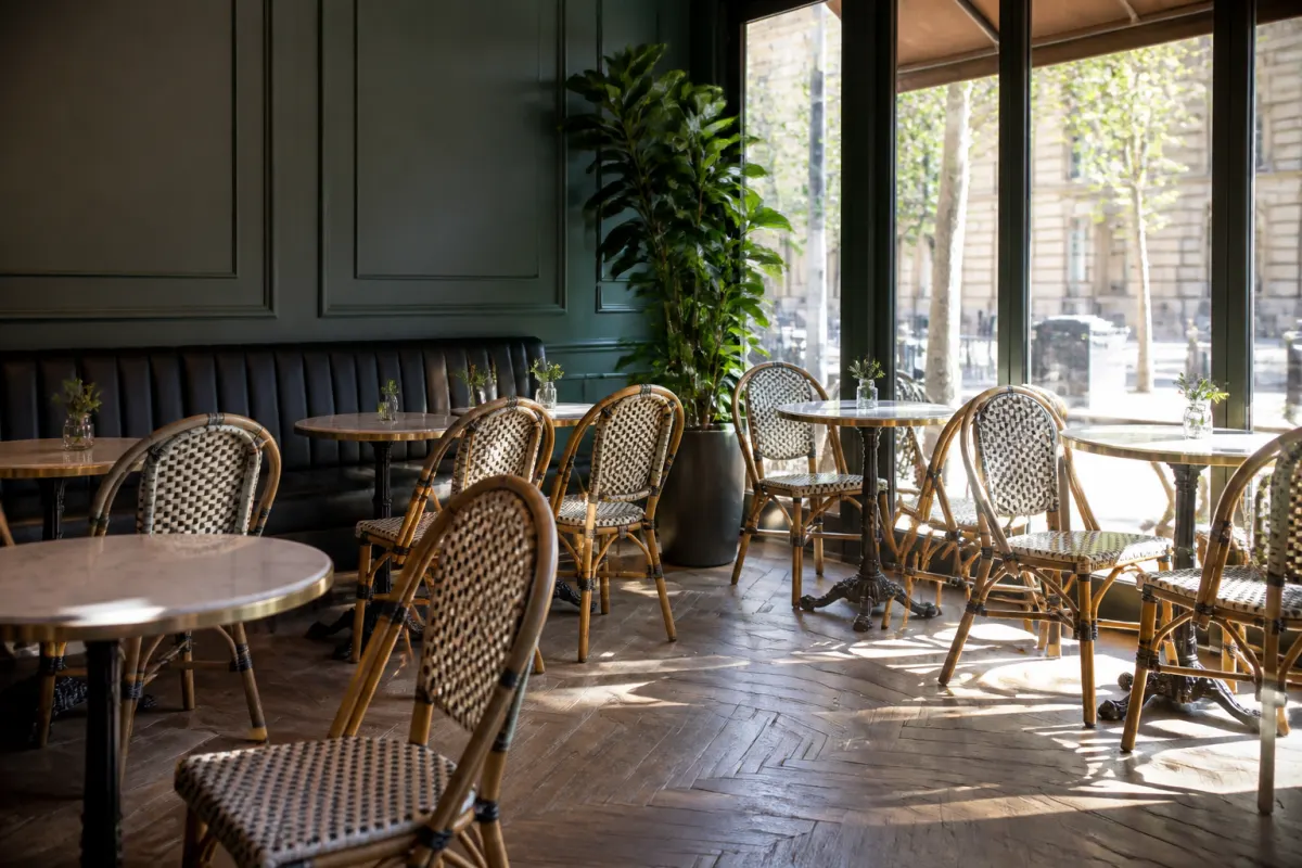 Parisian style cafe interior with generic woven bistro chairs and small round marble look tables, soft daylight