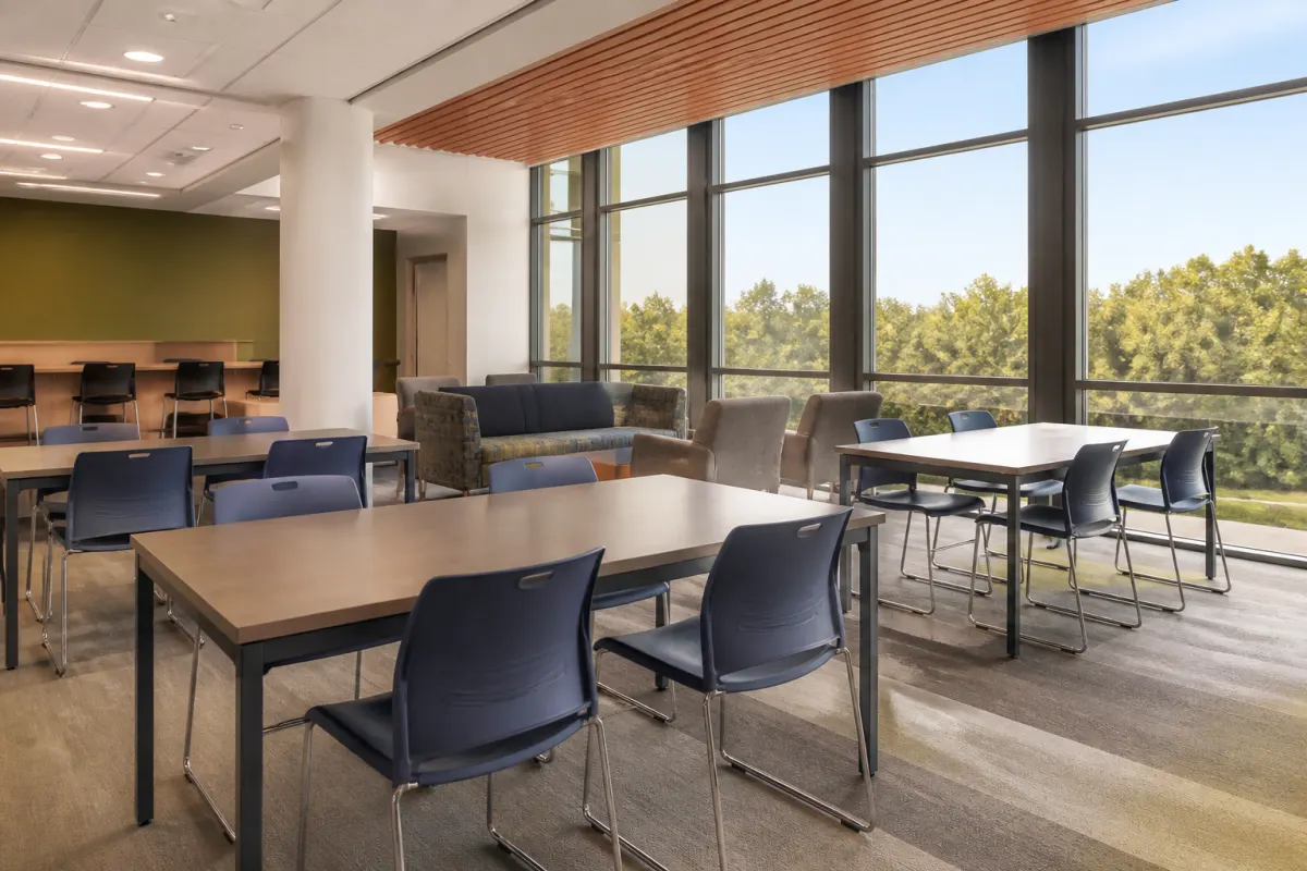 Dorm study lounge with sturdy tables and stackable chairs by large windows, clean modern finish